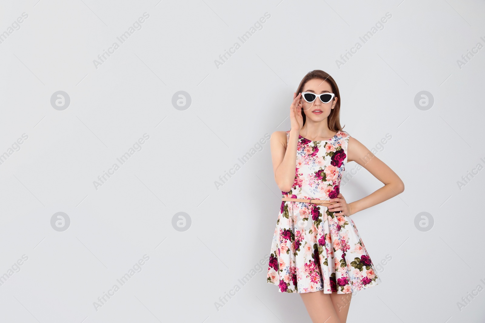 Photo of Young woman wearing floral print dress and stylish sunglasses on light background. Space for text