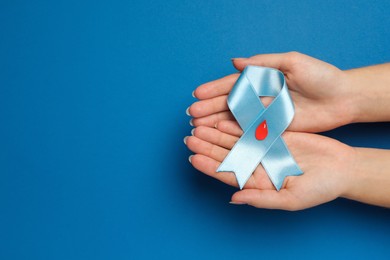 Photo of Woman holding light blue ribbon with paper blood drop on color background, top view and space for text. Diabetes awareness