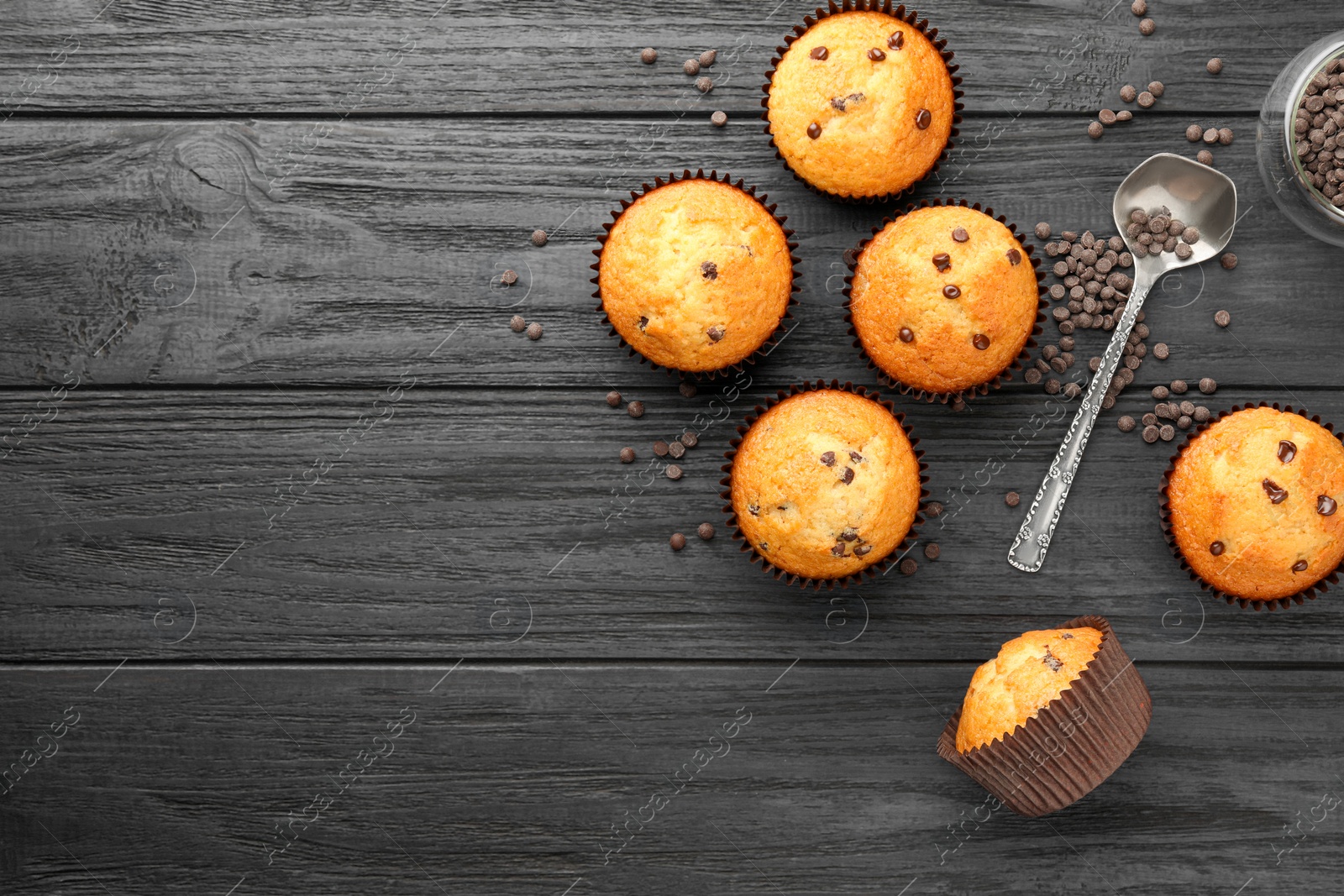 Photo of Delicious freshly baked muffins with chocolate chips on dark gray table, flat lay. Space for text