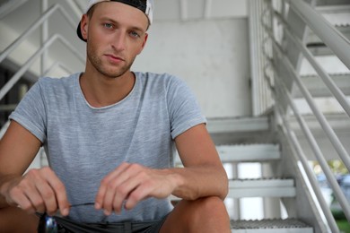 Photo of Handsome young man in stylish cap sitting on stairs outdoors. Space for text