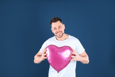 Portrait of young man with heart shaped balloon on color background