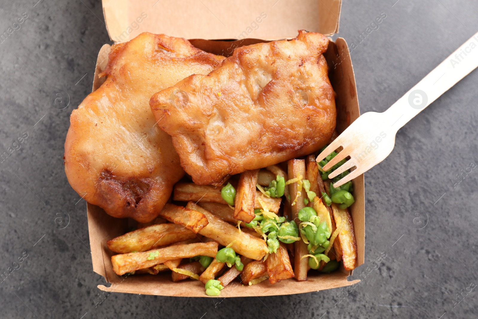 Photo of Tasty fish, chips and peas in paper box on grey table, top view