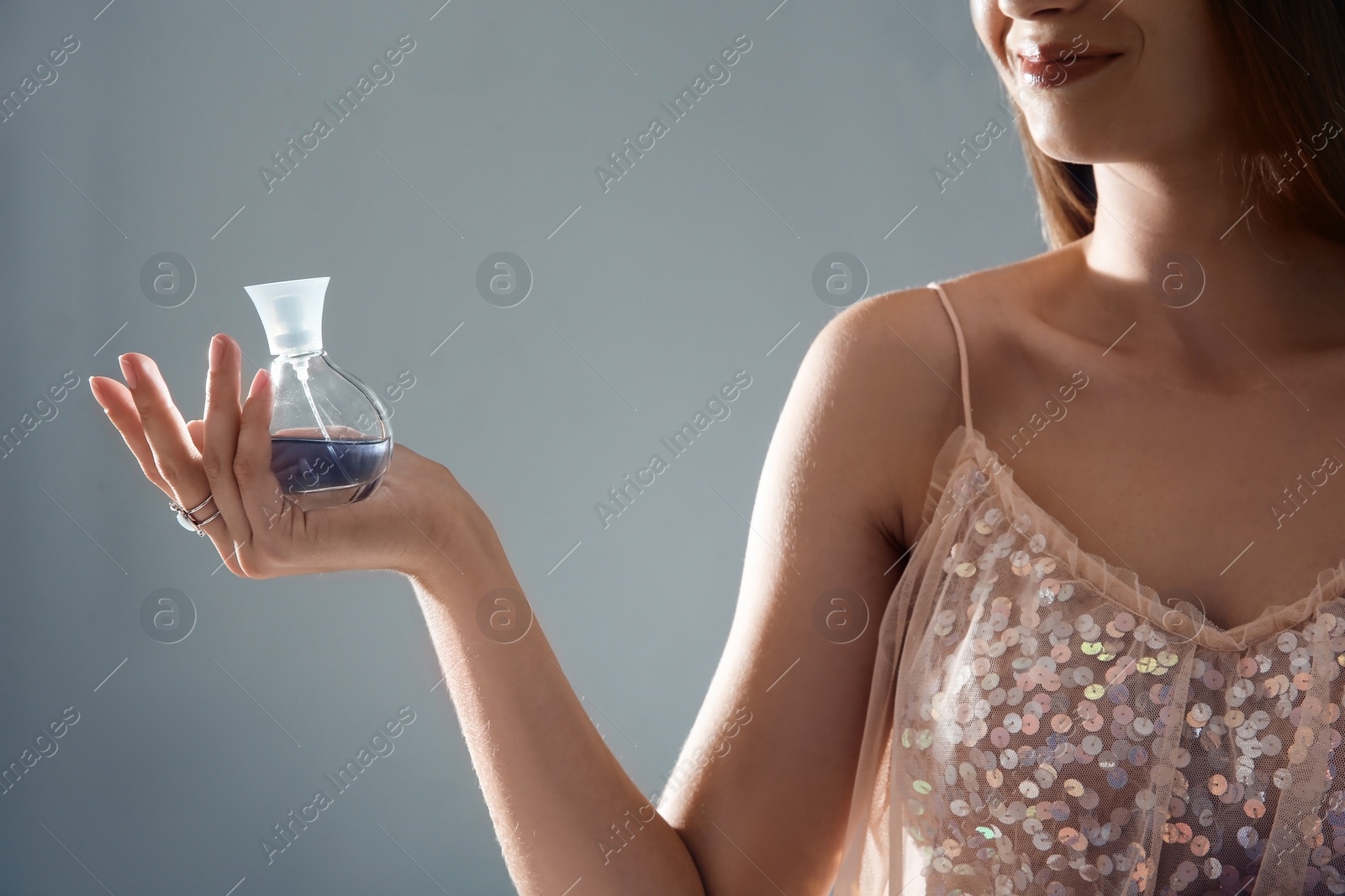 Photo of Young woman with perfume bottle on gray background, closeup