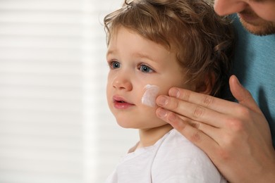 Photo of Father applying ointment onto his son`s cheek on blurred background. Space for text