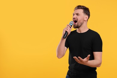 Handsome man with microphone singing on yellow background. Space for text