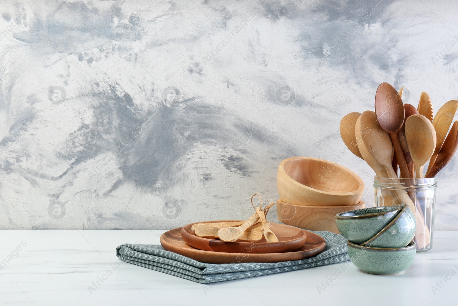 Photo of Different dishware and utensils on white marble table against textured wall. Space for text