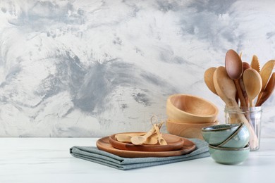 Photo of Different dishware and utensils on white marble table against textured wall. Space for text