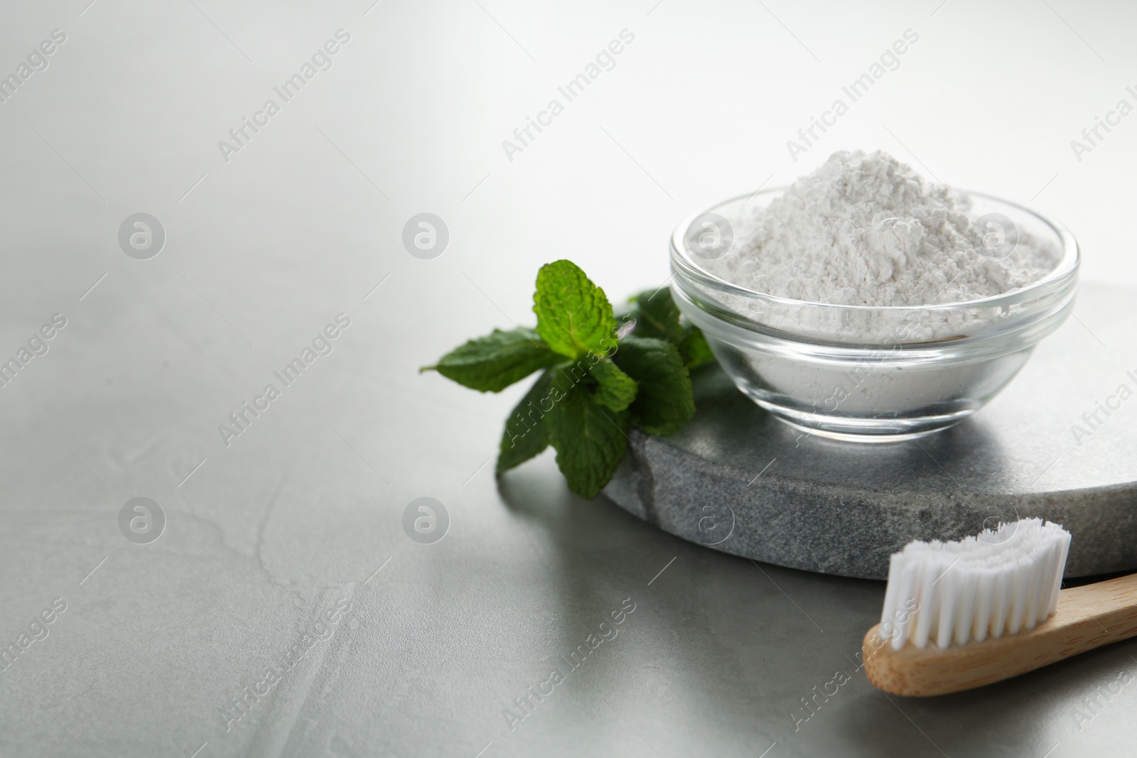 Photo of Tooth powder, brush and mint on grey table, space for text