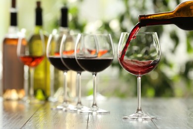 Photo of Pouring red wine from bottle into glass on wooden table