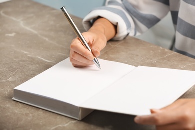 Photo of Writer signing autograph in book at table, closeup