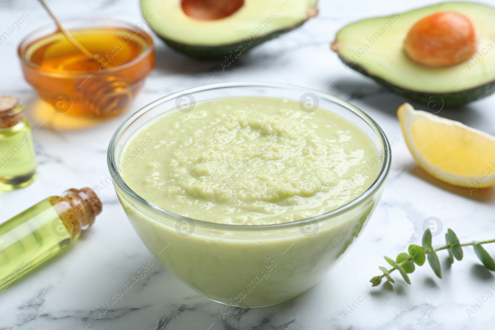 Photo of Homemade hair mask in bowl and ingredients on white marble table, closeup