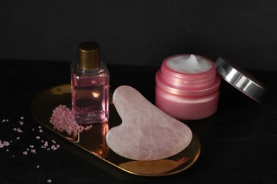 Photo of Rose quartz gua sha tool and cosmetic products on black table