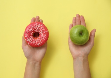Photo of Top view of woman choosing between doughnut and healthy apple on yellow background, closeup