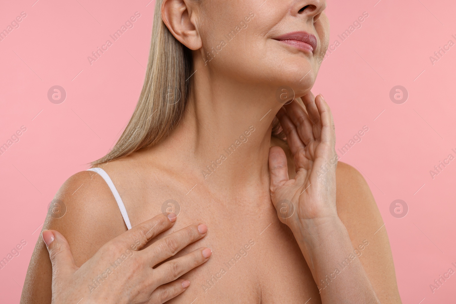 Photo of Mature woman touching her neck on pink background, closeup