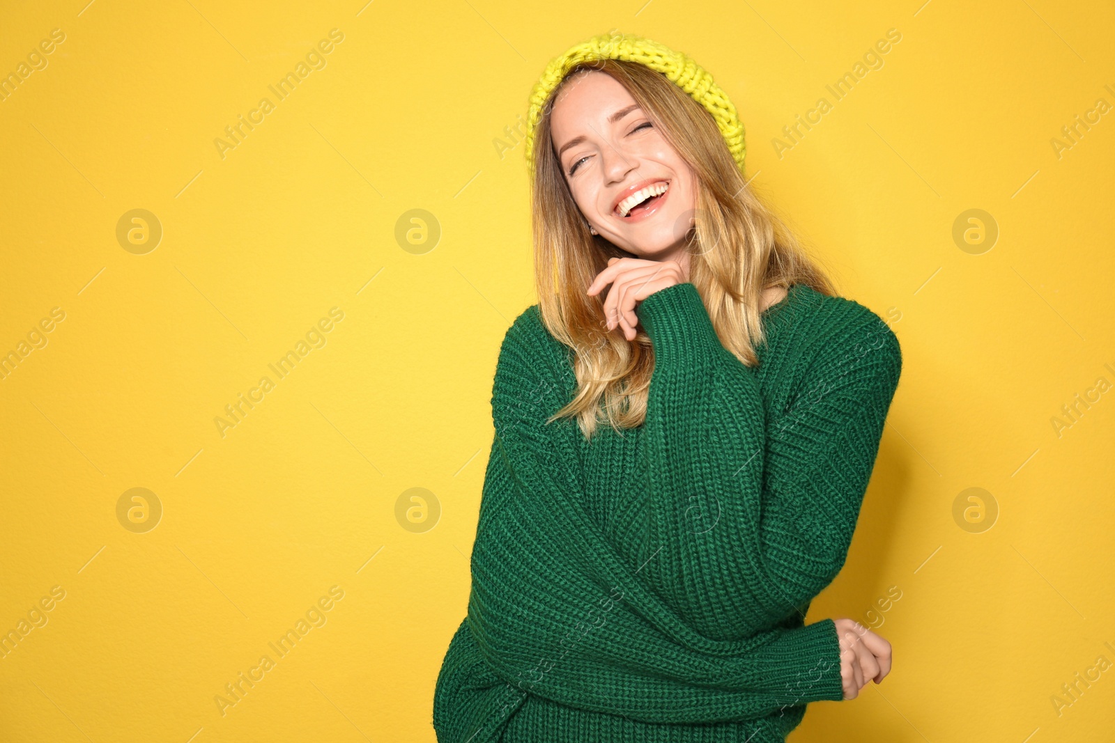 Image of Happy young woman wearing warm sweater and knitted hat on yellow background