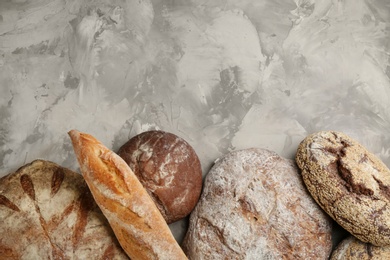 Photo of Different kinds of fresh bread on grey table, flat lay. Space for text