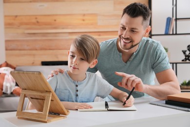 Photo of Boy with father doing homework using tablet at table in living room