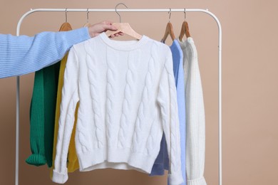 Woman holding hanger with knitted sweater against beige background, closeup