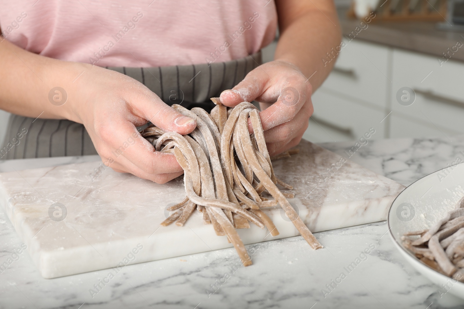 Photo of Woman making soba (buckwheat noodles) at white marble table in kitchen, closeup