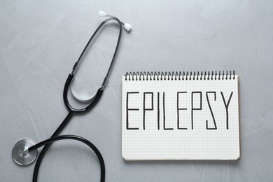 Photo of Notebook with word Epilepsy and stethoscope on grey table, flat lay