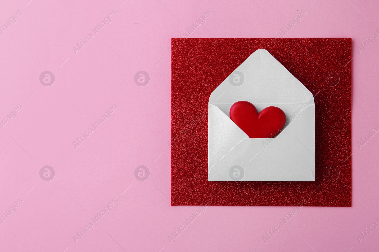 Photo of Composition with white envelope and red wooden heart on pink background, top view. Space for text