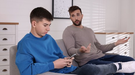 Photo of Boy using smartphone and ignoring his upset father at home. Teenager problems