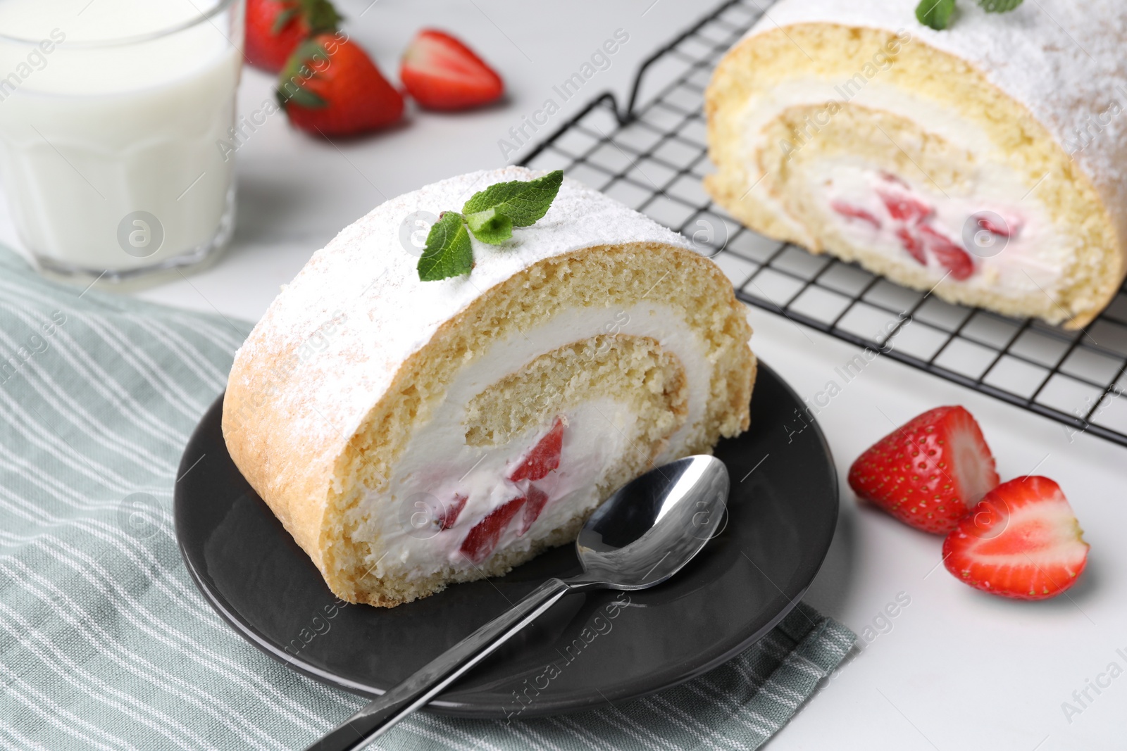 Photo of Slice of delicious sponge cake roll with strawberries and cream served on white table