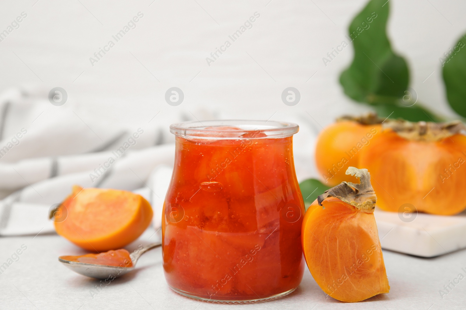 Photo of Jar of tasty persimmon jam, ingredients on white table