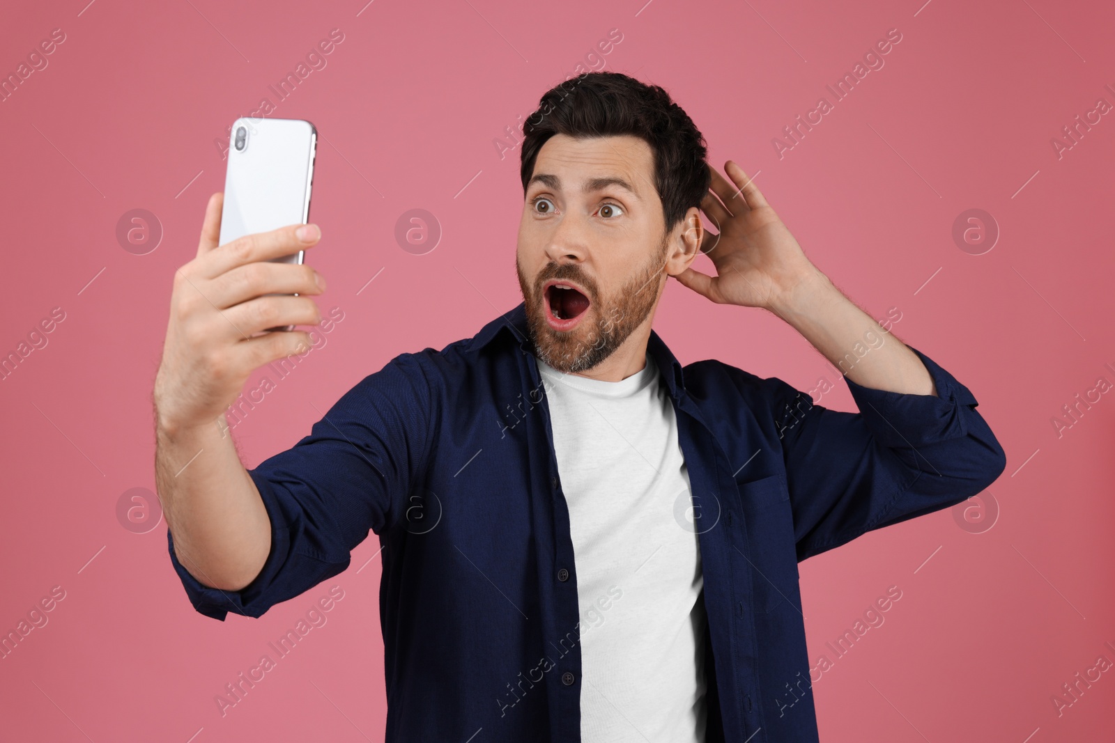 Photo of Surprised man taking selfie with smartphone on pink background