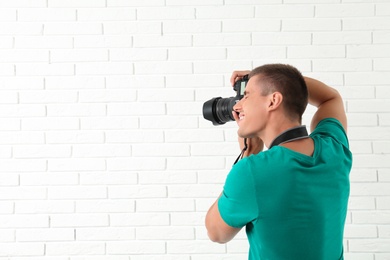 Young professional photographer taking picture near brick wall. Space for text