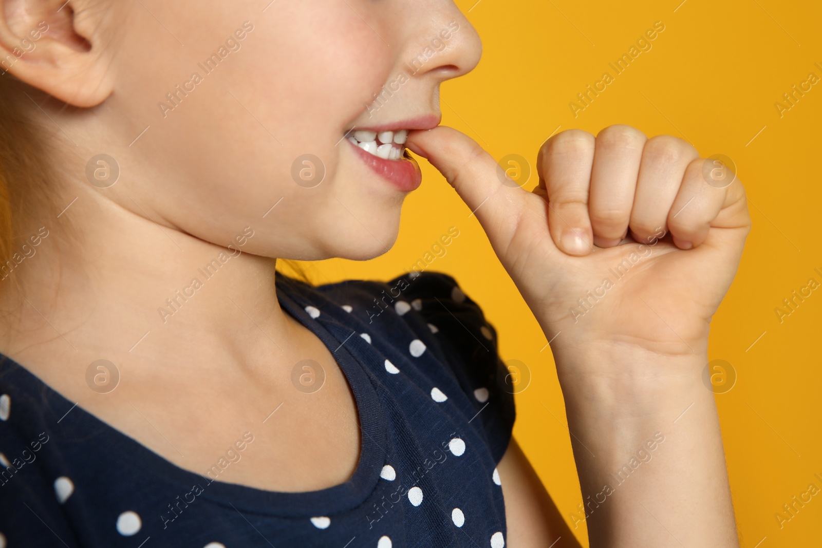 Photo of Little girl biting her nails on orange background, closeup