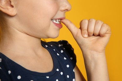 Little girl biting her nails on orange background, closeup