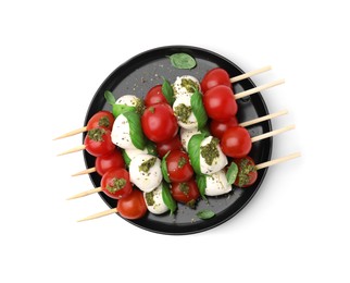 Plate of Caprese skewers with tomatoes, mozzarella balls, basil and pesto sauce isolated on white, top view