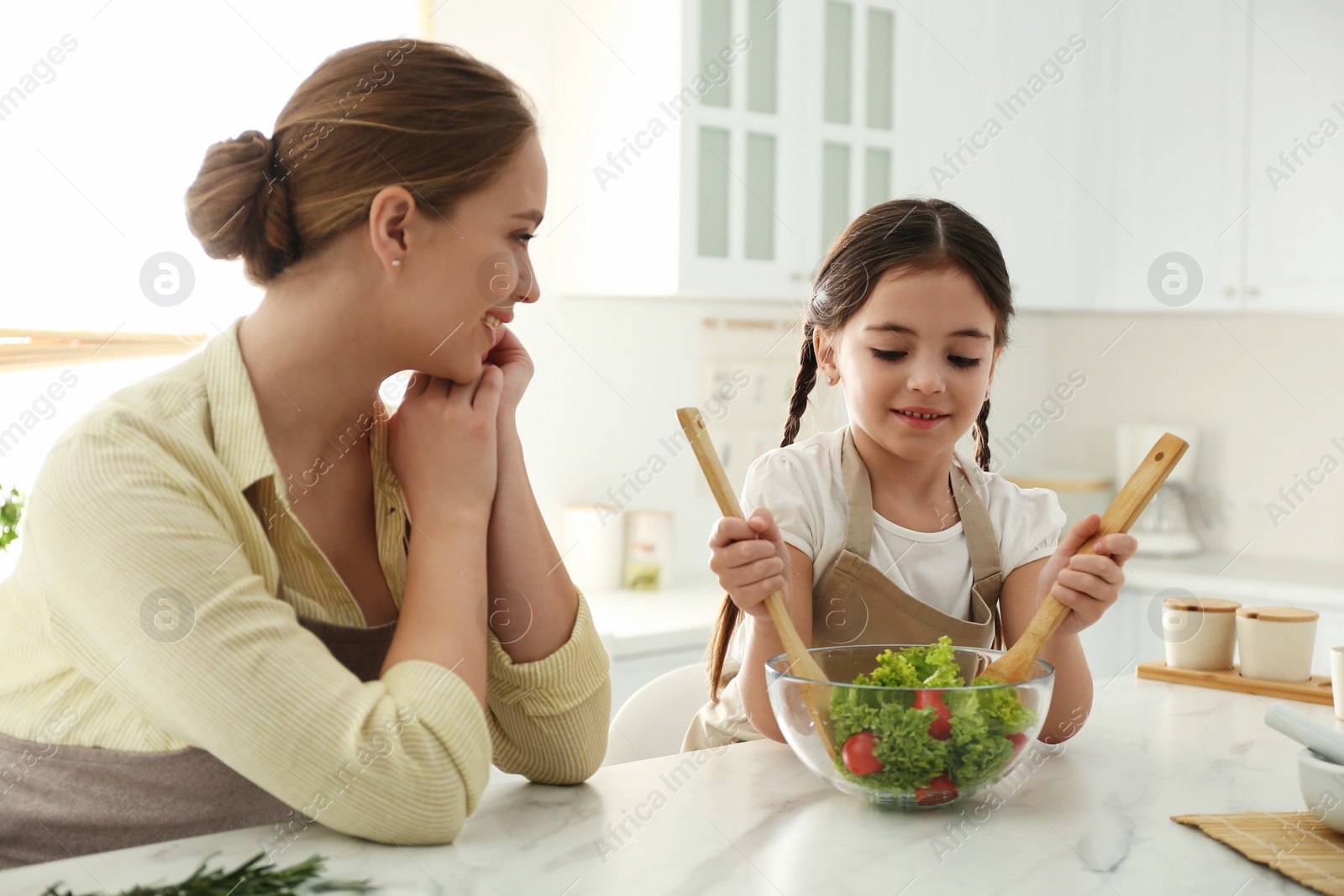 Photo of Mother and daughter cooking salad together in kitchen