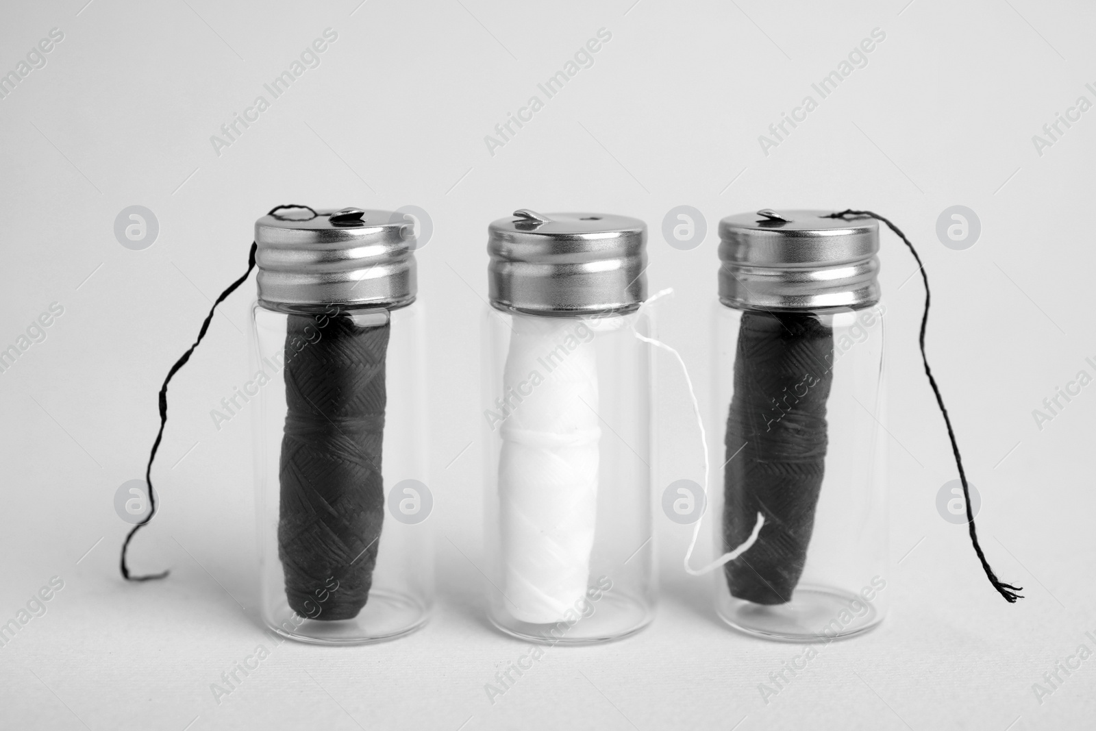 Photo of Biodegradable dental flosses in glass jars on light background