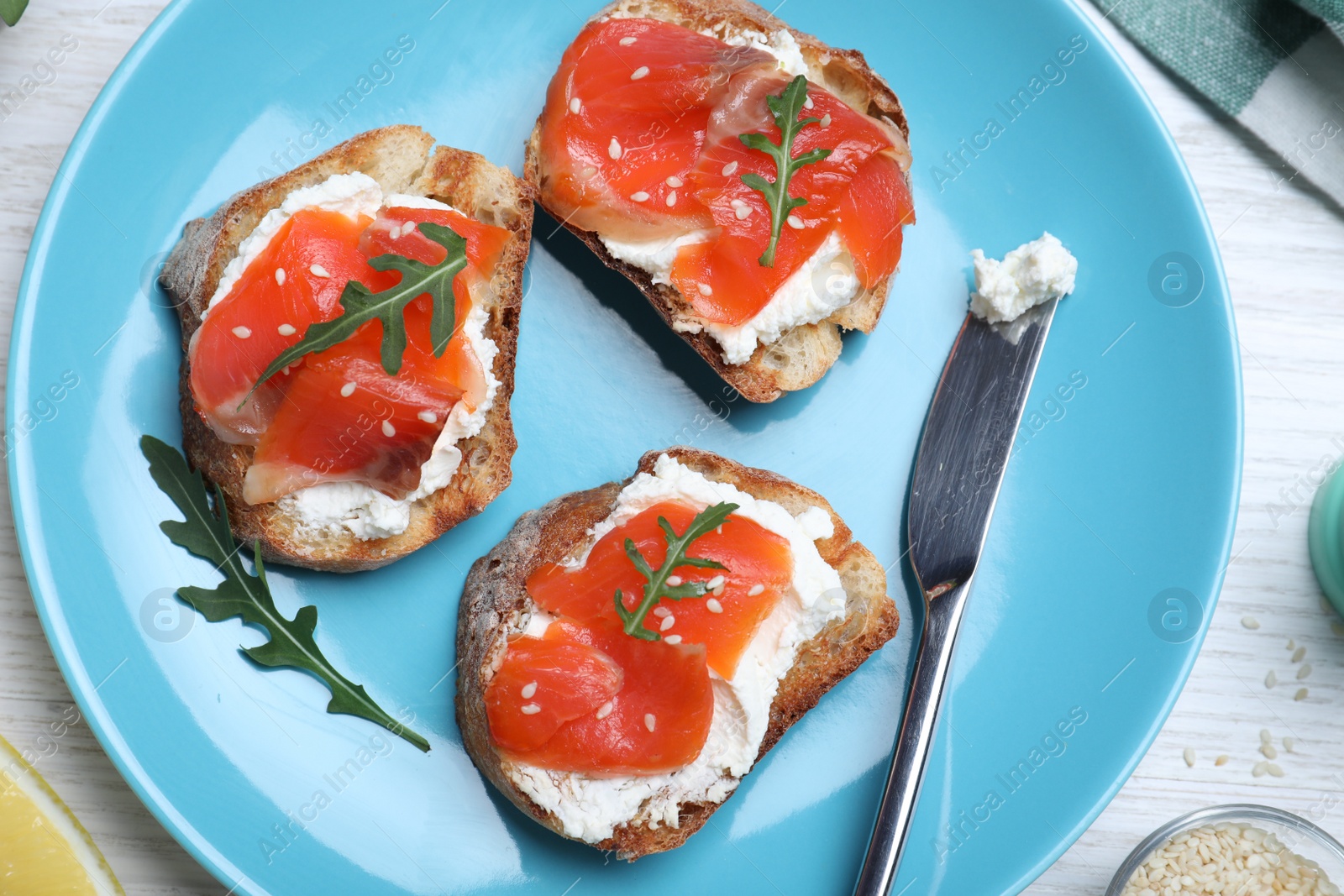 Photo of Delicious sandwiches with cream cheese, salmon and arugula served on white wooden table, flat lay