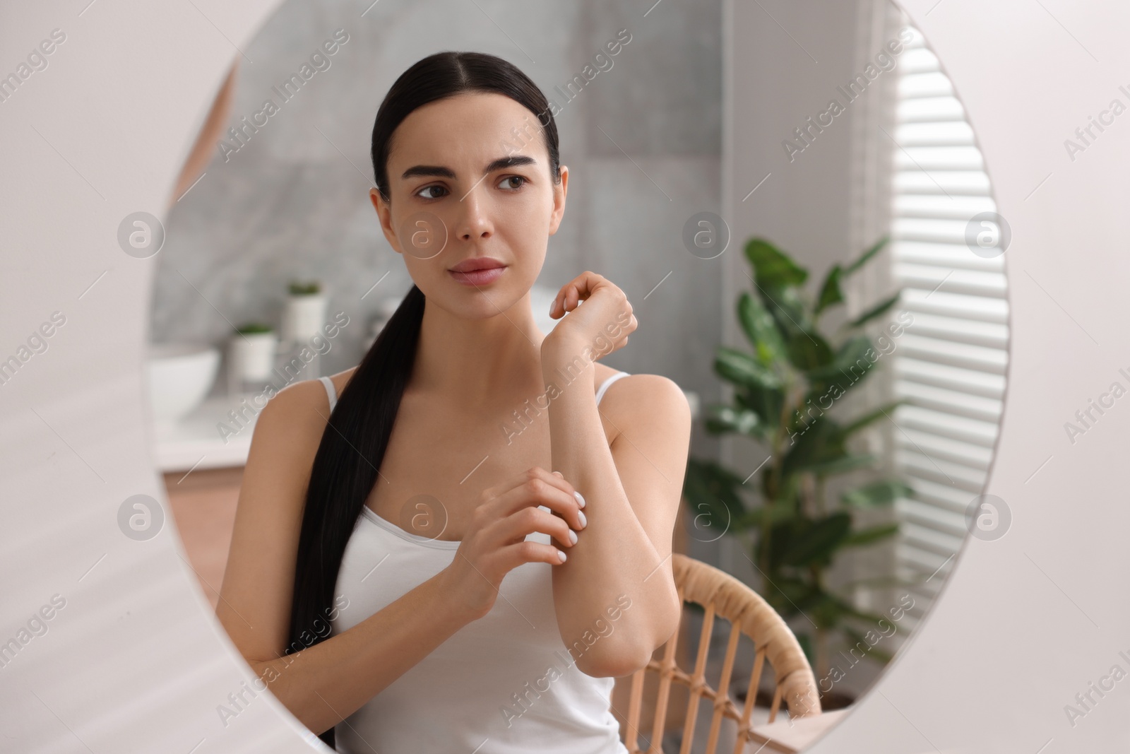 Photo of Woman with dry skin looking at mirror in bathroom