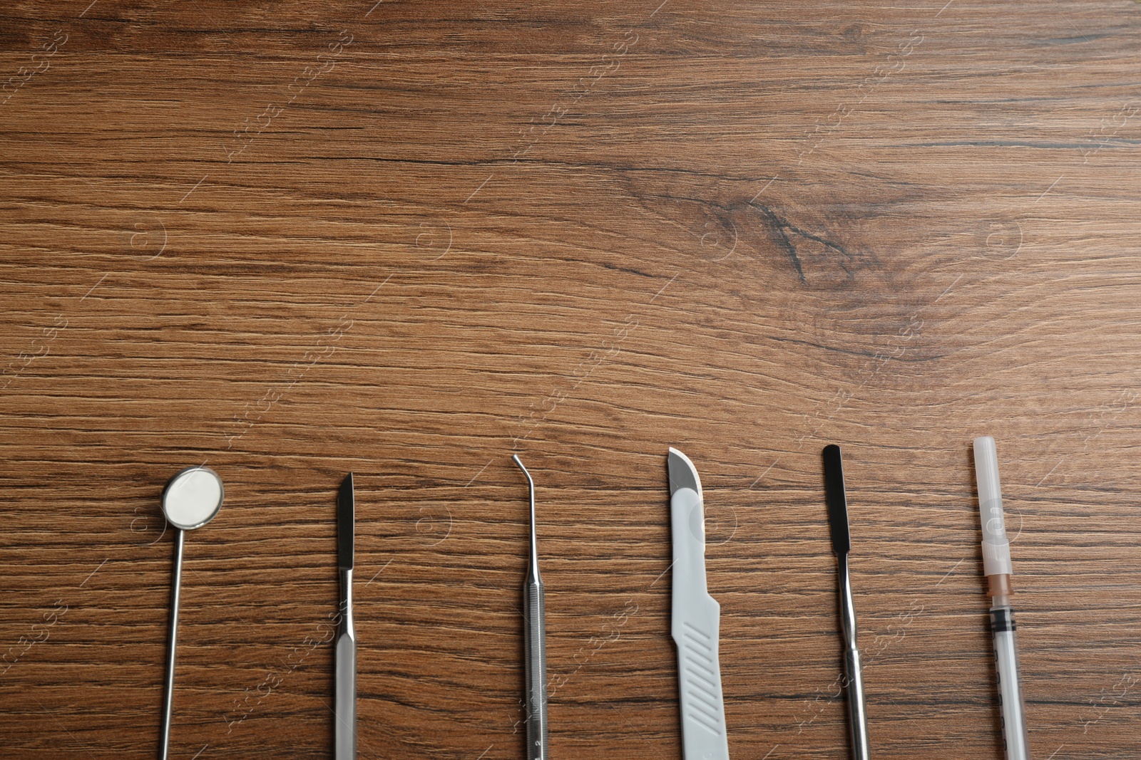 Photo of Set of different dentist's tools and syringe on wooden table, flat lay. Space for text