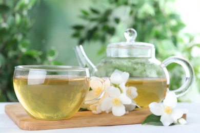 Photo of Tasty tea and fresh jasmine flowers on white wooden table