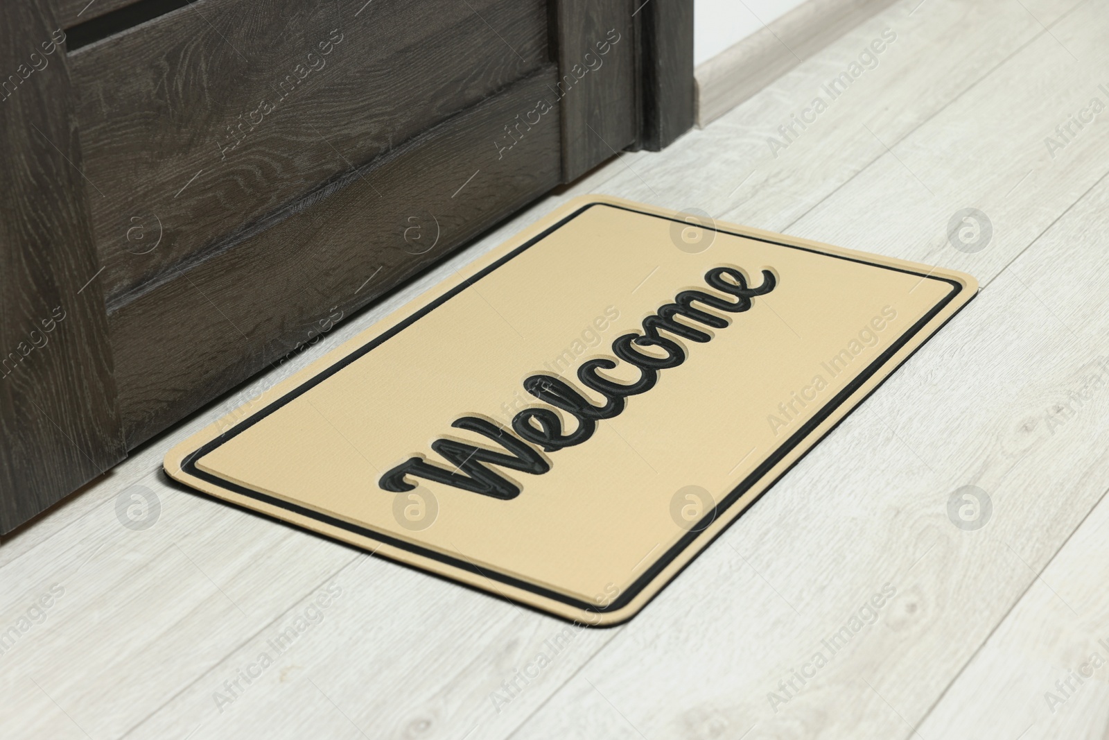 Photo of Beige doormat with word Welcome on white floor near entrance