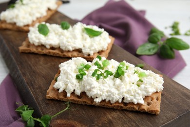 Photo of Crispy crackers with cottage cheese and different herbs on wooden board, closeup