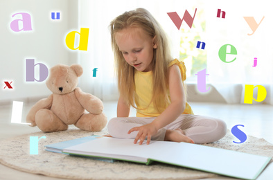 Pretty little girl reading book on floor in room