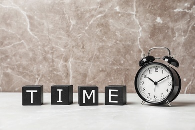 Alarm clock and cubes with word TIME on table