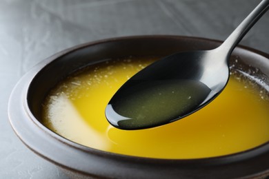 Photo of Spoon of clarified butter over bowl on black table, closeup