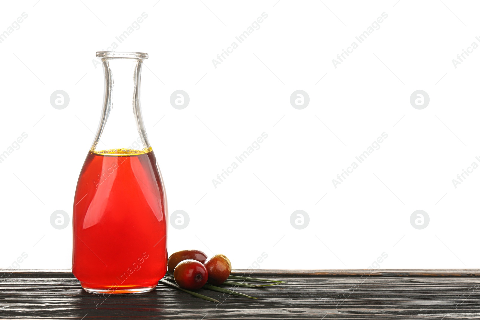 Photo of Palm oil in glass bottle and fruits on wooden table against white background