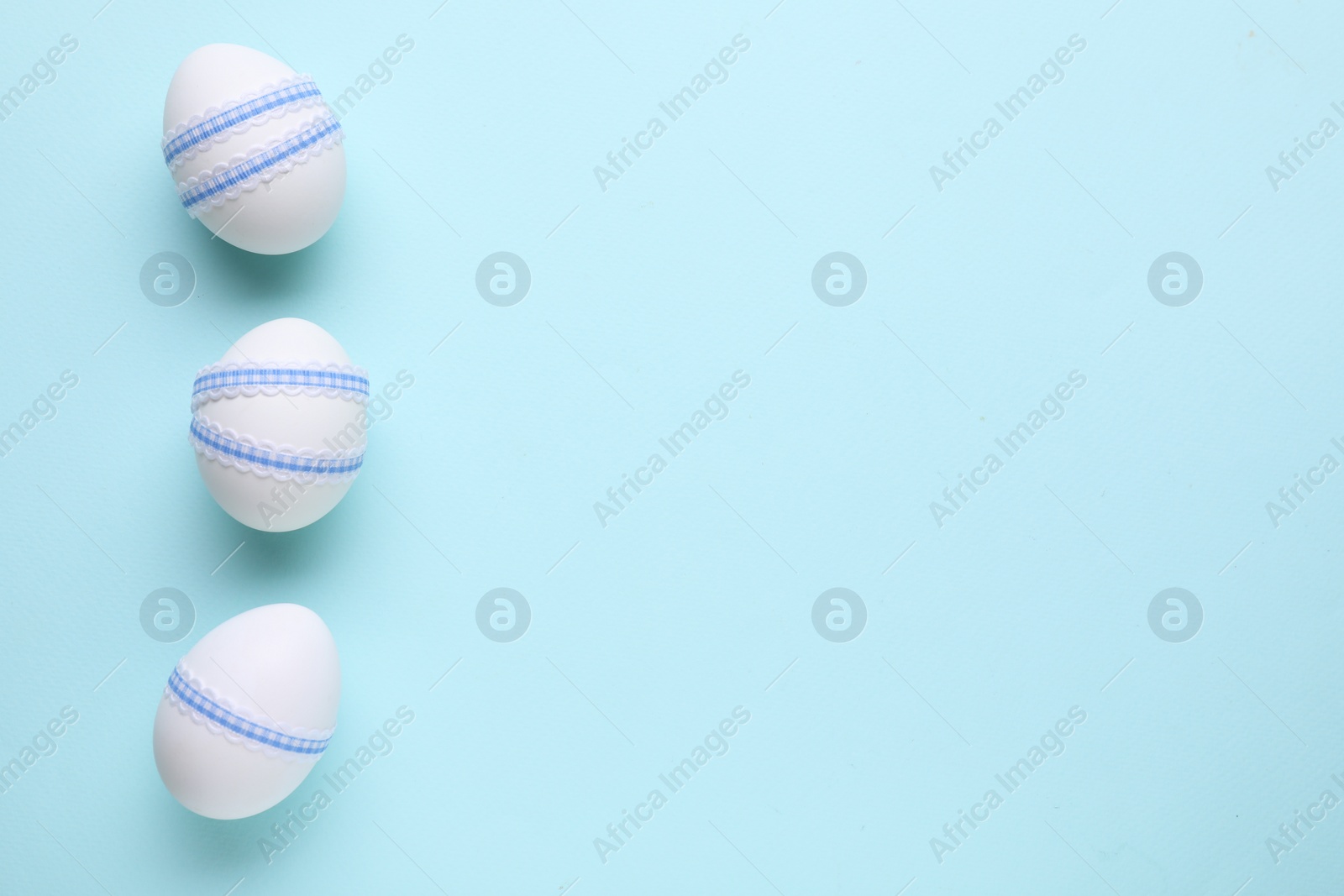 Photo of Festively decorated Easter eggs on light blue background, top view. Space for text