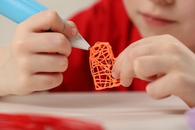 Photo of Boy drawing with stylish 3D pen at white table, closeup