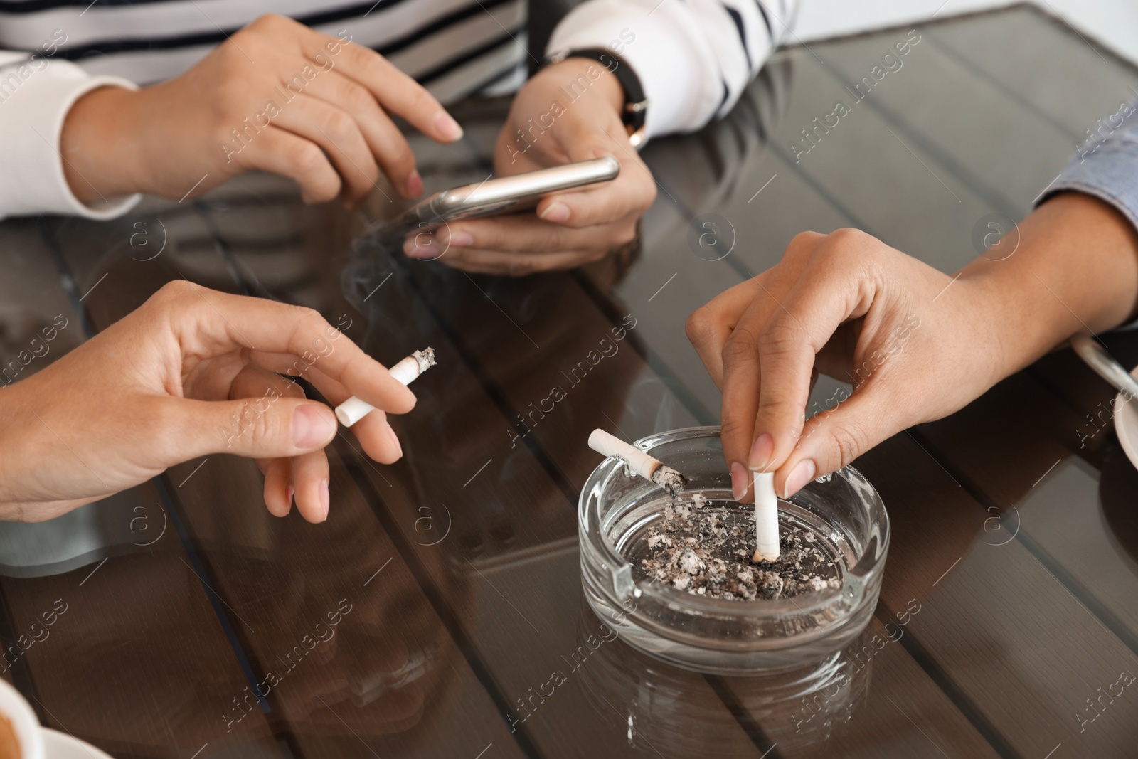 Photo of Woman putting out cigarette in ashtray at table, closeup