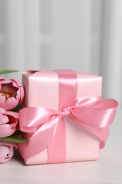 Photo of Beautiful gift box with bow and pink tulip flowers on white table, closeup