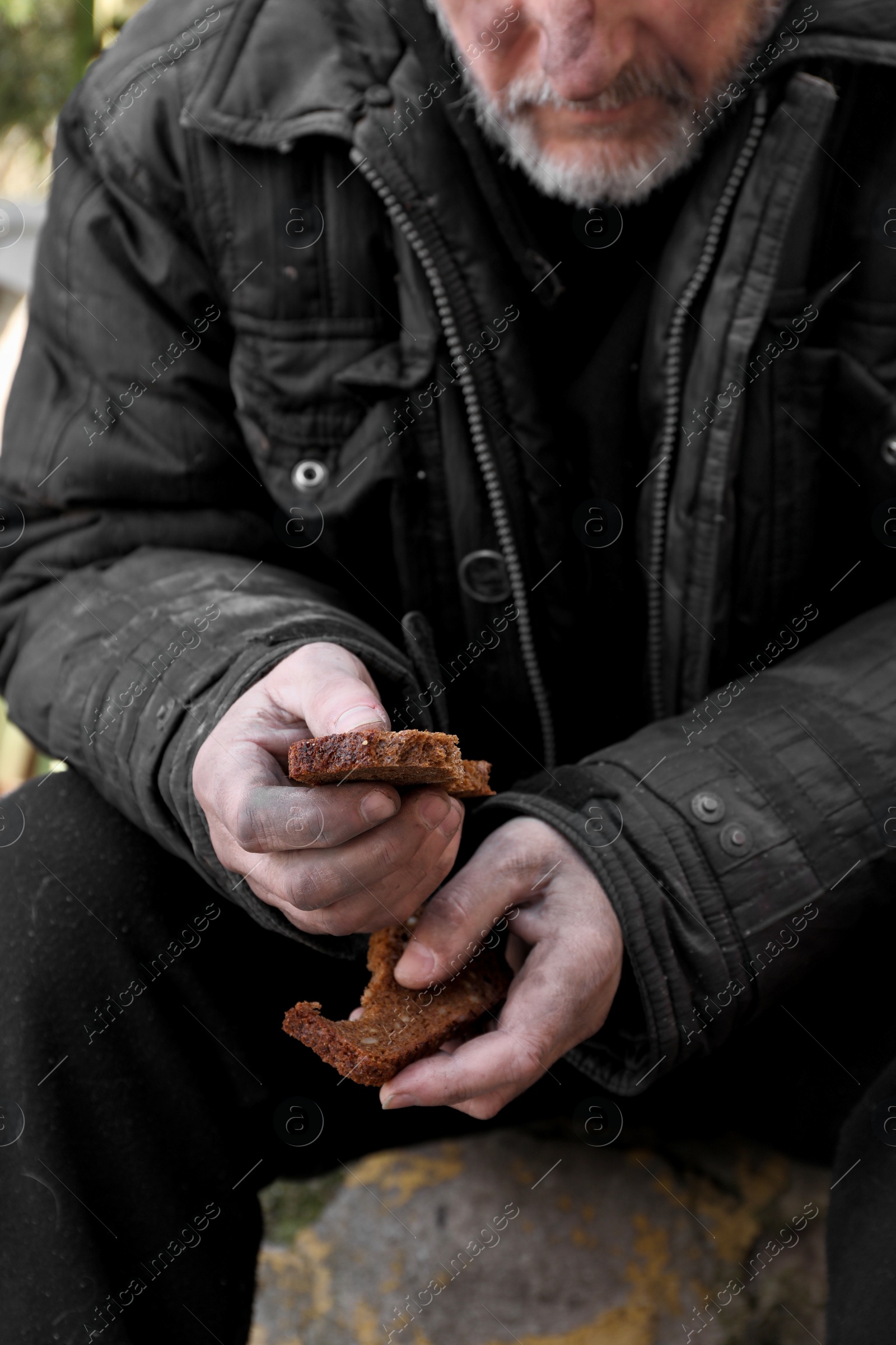 Photo of Poor homeless man holding piece of bread outdoors